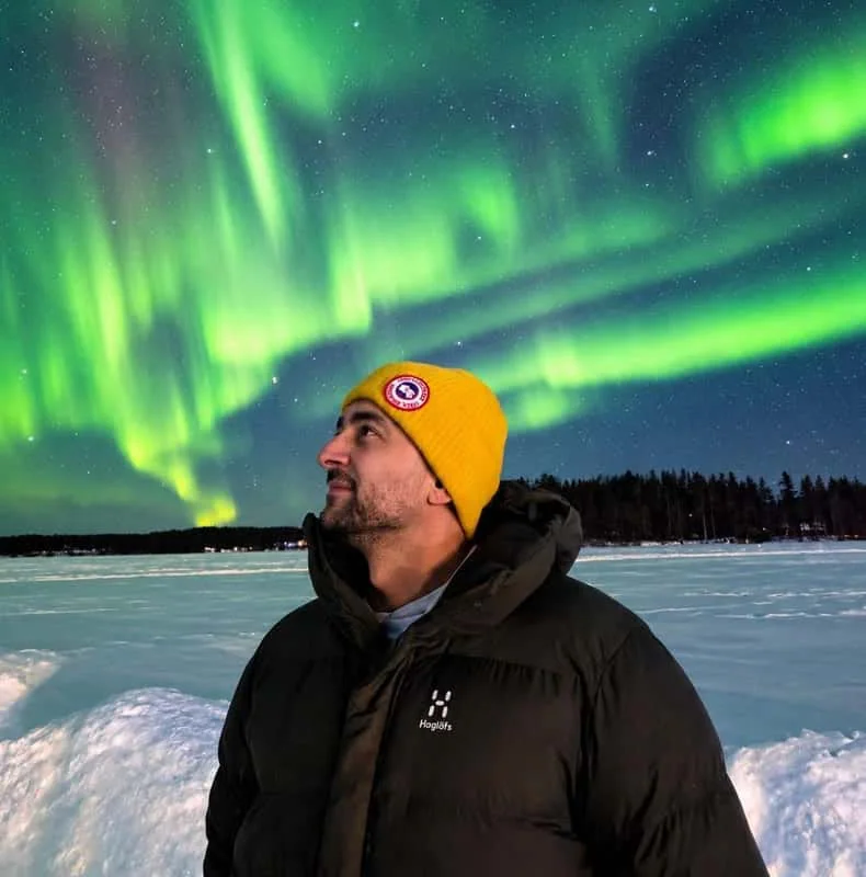 LAT Aurora guide beneath green Northern Lights on a frozen lake near Rovaniemi